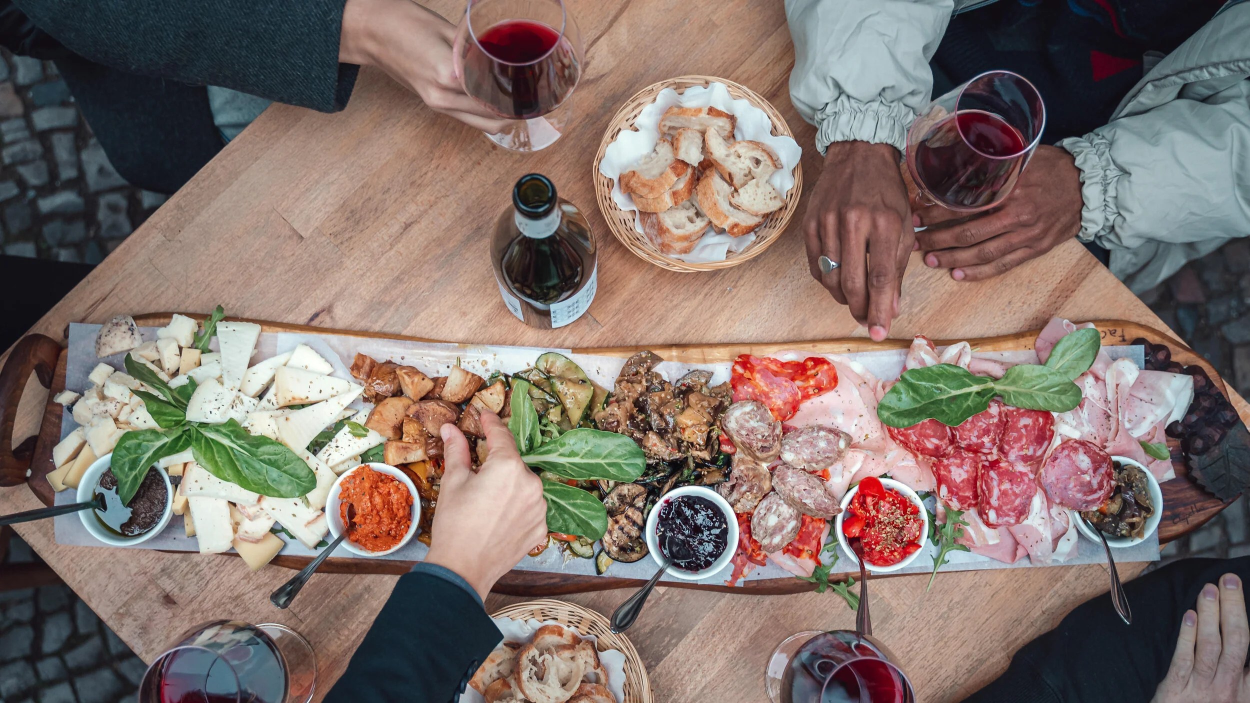 Friends sharing Italian antipasti and red wine around a table at Facciola